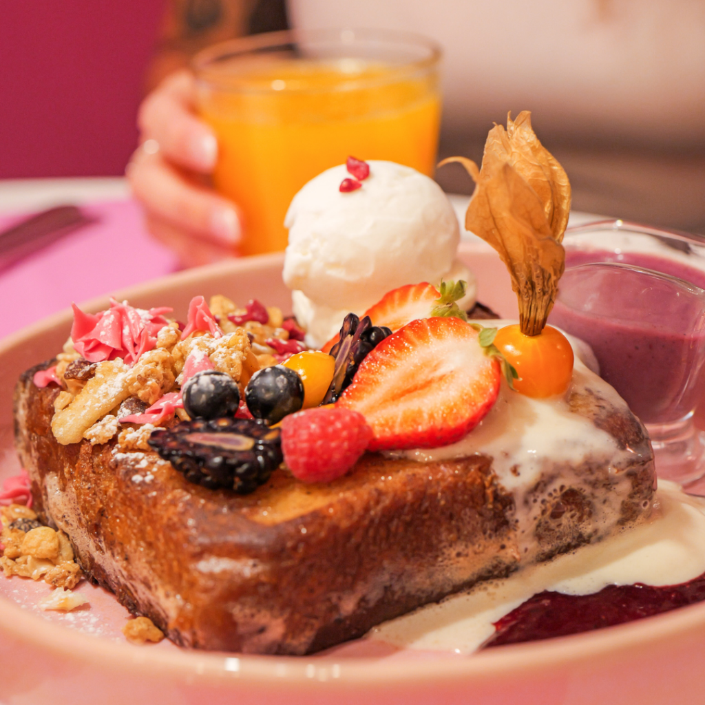 French Toast de Berry Brunch: pan brioche con mermelada de frutos rojos, crema fraîche, granola y fruta fresca, servido en un plato vibrante y colorido.